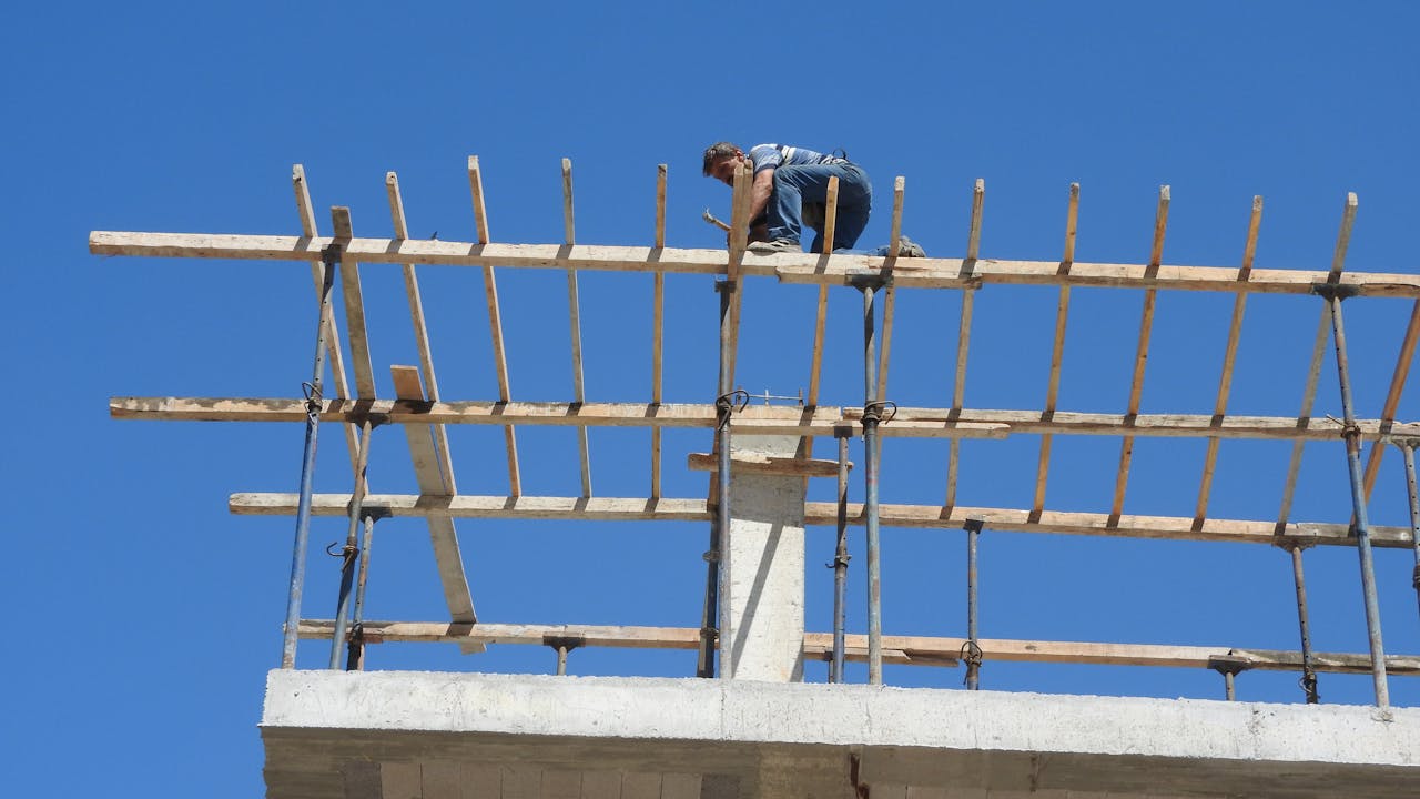 A construction worker skillfully balances on high scaffolding against a clear blue sky.