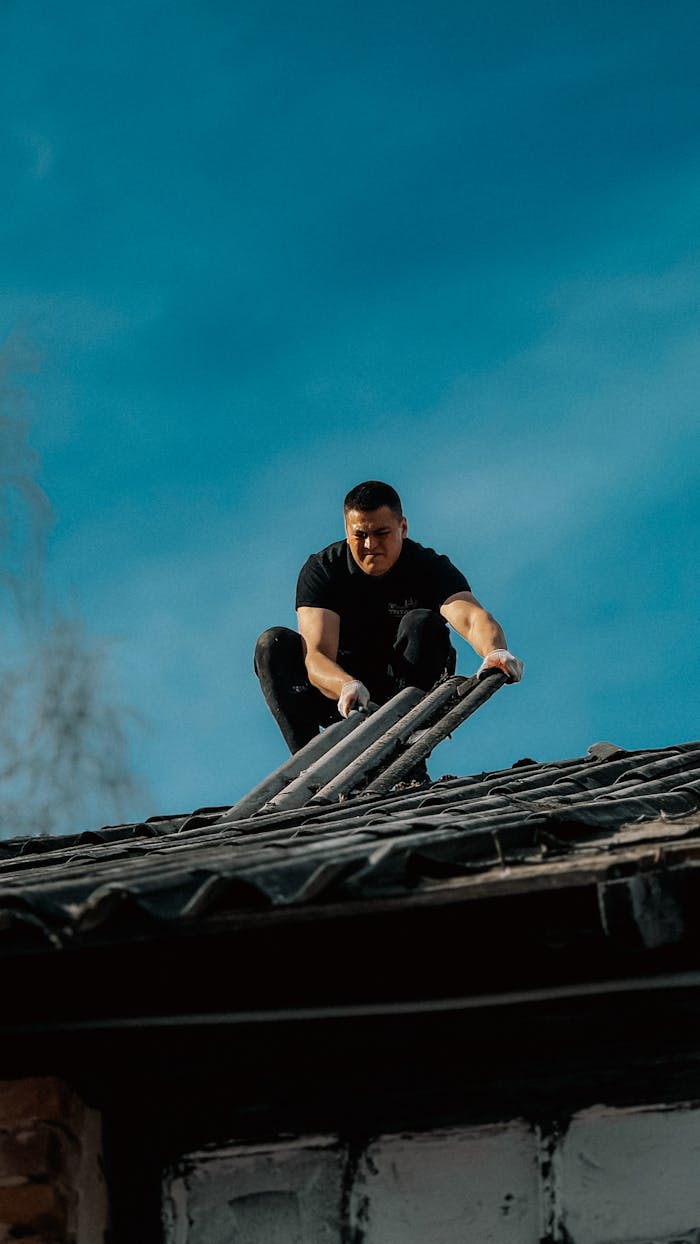 A man climbs a ladder onto a rooftop under a clear blue sky, focusing on safety and construction.