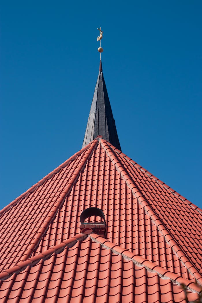 A striking red brick roof of a church with a pointed spire under a clear blue sky.